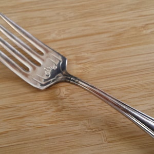 Könnte beinhalten: Eine silberne Gabel mit einem dekorativen Design am Griff. Die Gabel liegt auf einer Holzoberfläche.