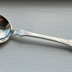 Puede incluir: Una cuchara de plata con un diseño floral adornado en el mango. La cuchara tiene un cuenco redondeado y un acabado pulido.