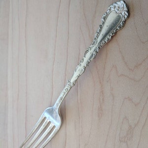 Könnte beinhalten: Eine silberne Gabel mit einem verzierten Griff und einem dekorativen Design. Die Gabel hat vier Zinken und ist in gutem Zustand.