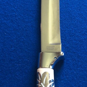 May include: A silver knife with a white handle featuring a floral design. The blade is marked "STAINLESS SOLINGEN GERMANY".