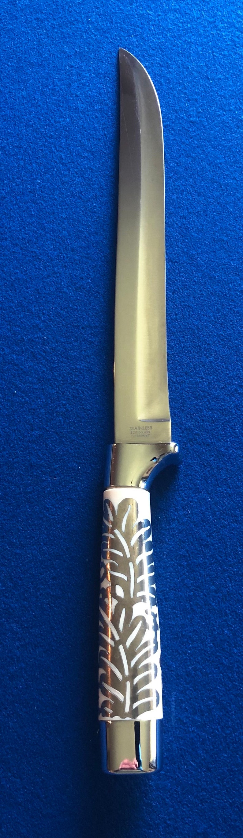 May include: A silver knife with a white handle featuring a floral design. The blade is marked "STAINLESS SOLINGEN GERMANY".