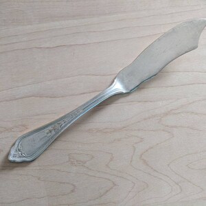 May include: A silver butter knife with an ornate handle. The blade is slightly curved and the handle has a floral design.