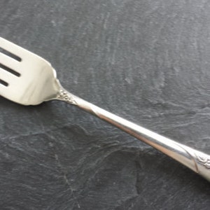 Puede incluir: Un tenedor de plata con un diseño floral decorativo en el mango. El tenedor tiene cuatro dientes y un acabado pulido.