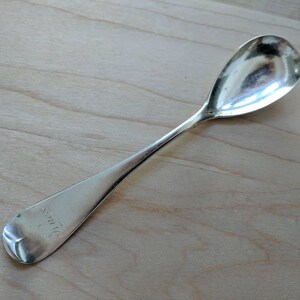 May include: A silver teaspoon with a rounded bowl and a long, slender handle. The handle is engraved with the word "W.H.C."