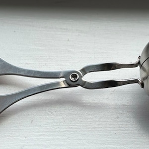 May include: A silver metal ball scoop with a handle that has two loops. The scoop is designed to make perfectly round balls of food.