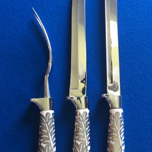 May include: Three silver knives with white handles featuring a floral design. The knives have different blade shapes and sizes.