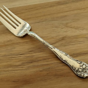 以下が含まれることがあります： ハンドルに装飾的な花柄が施された銀製のフォーク。フォークは4本の歯と磨かれた仕上げになっています。