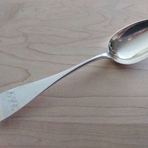 Puede incluir: Una cuchara de plata con un cuenco ovalado y un mango largo y delgado. El mango está grabado con las iniciales "S.W."