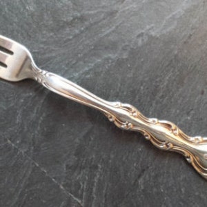 Può includere: Una forchetta d'argento con un manico decorato. La forchetta ha tre rebbi e un design decorativo sul manico.