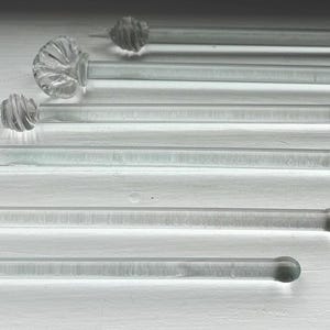 May include: Set of seven clear glass stirring sticks with decorative glass knobs on one end. The knobs have a scalloped design.