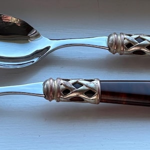 May include: Two silver spoons with dark brown handles. The spoons have a shiny, reflective surface and a decorative silver band where the handle meets the spoon bowl. The handles are a rich, dark brown color.
