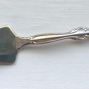 May include: A silver cake server with an ornate handle and a triangular blade.