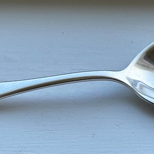 Puede incluir: Una cuchara de plata con un diseño adornado en el mango. La cuchara está ligeramente curvada y tiene un cuenco redondeado.