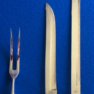 May include: A set of three silver-toned kitchen utensils with ivory-colored handles. The set includes a carving knife, a bread knife, and a fork. The handles have a floral design.