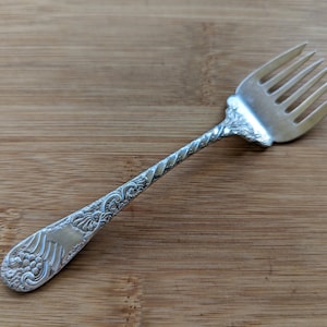 May include: A silver fork with an ornate, twisted handle. The handle is decorated with a floral design.