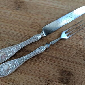 May include: A silver knife and fork with ornate handles. The knife has a plain blade and the fork has three tines.