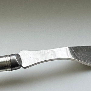 Puede incluir: Un tenedor de servir de plata con mango de nácar. El tenedor tiene dos púas y un mango curvo.