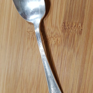 May include: A silver teaspoon with an ornate handle featuring a woman's profile and the inscription "The Wilcox".