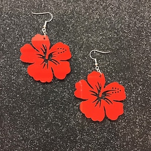 May include: A pair of red hibiscus flower earrings. The earrings are made of acrylic and have a shiny finish.