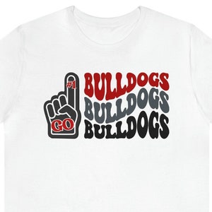May include: White t-shirt with a red, gray, and black graphic design. The graphic features a raised fist with the number "#1" on the index finger and the words "GO BULLDOGS" repeated three times.