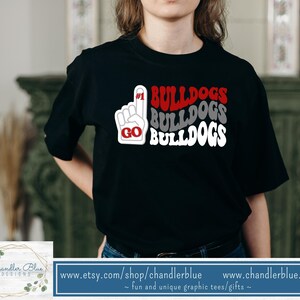 May include: Black t-shirt with a white graphic design that says "#1 BULLDOGS BULLDOGS BULLDOGS" with a red "GO" in a hand gesture.
