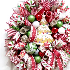 Puede incluir: Una festiva corona navide&ntilde;a con cintas, adornos y un &aacute;rbol de jengibre rojos, blancos y verdes. La corona presenta diversas texturas y patrones, creando una alegre decoraci&oacute;n navide&ntilde;a.