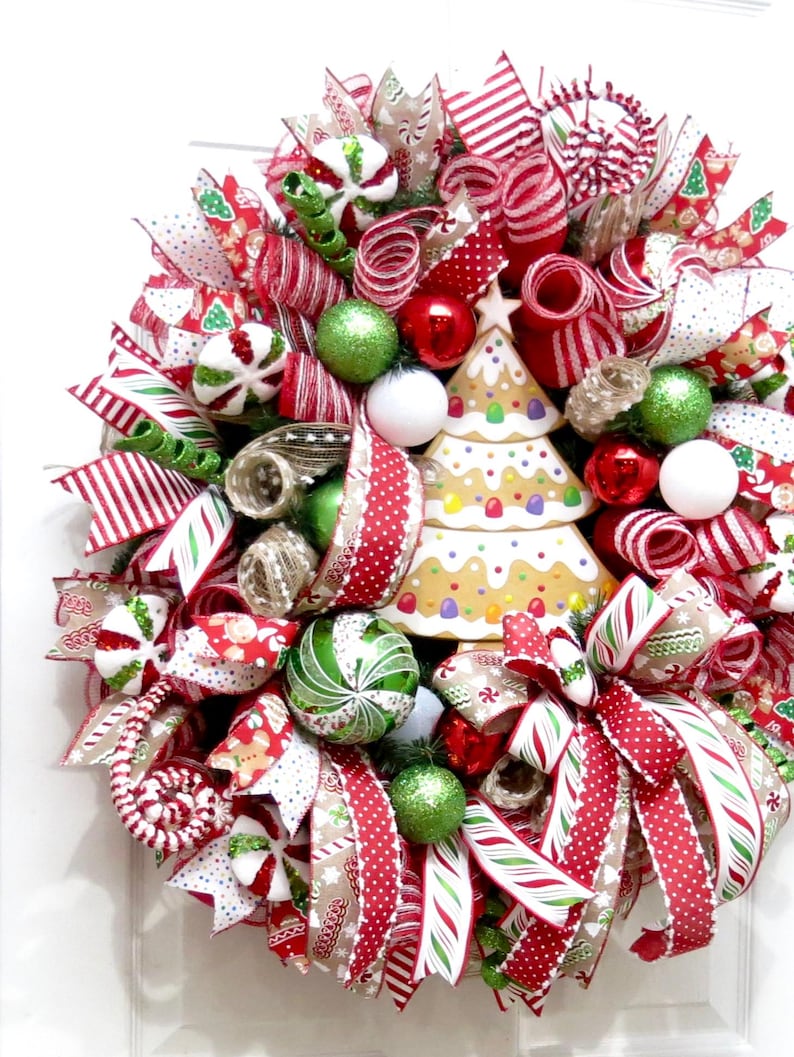 Puede incluir: Una festiva corona navide&ntilde;a con cintas, adornos y un &aacute;rbol de jengibre rojos, blancos y verdes. La corona presenta diversas texturas y patrones, creando una alegre decoraci&oacute;n navide&ntilde;a.
