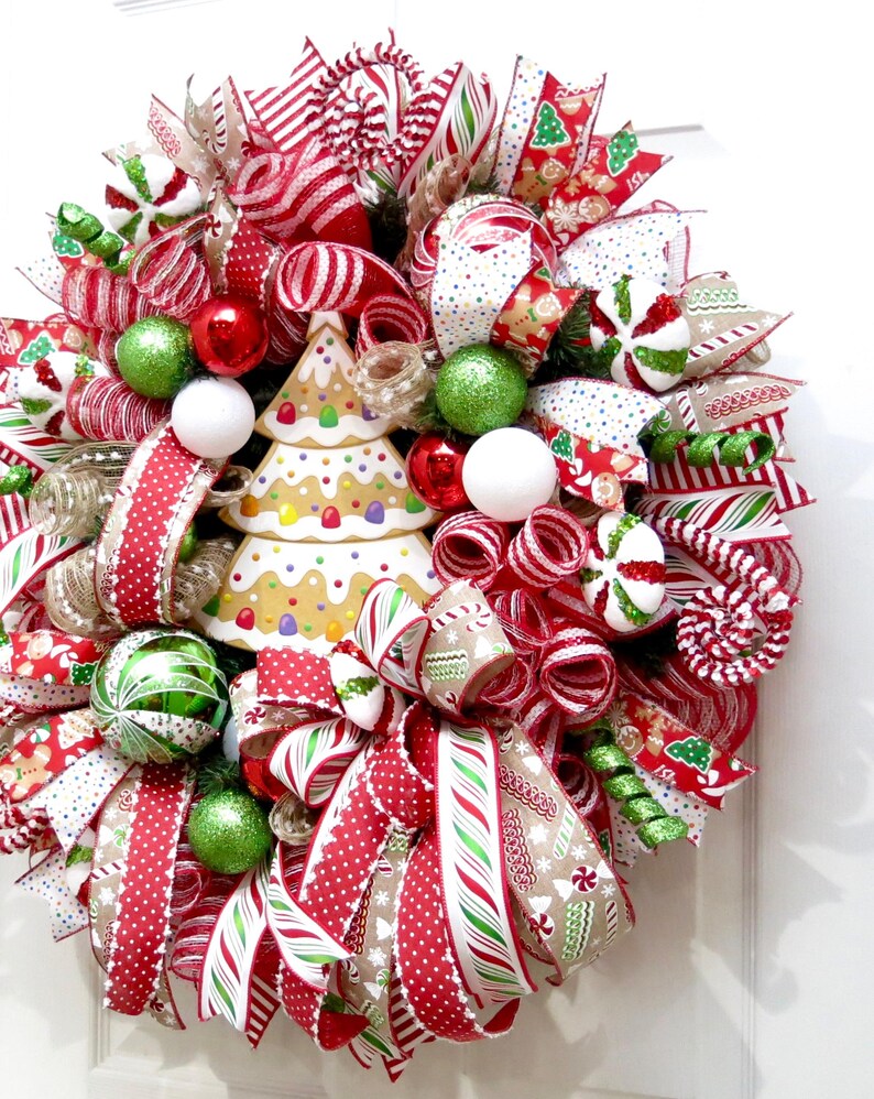 Puede incluir: Una festiva corona navide&ntilde;a con un centro de mesa de &aacute;rbol de pan de jengibre. La corona presenta cintas a rayas rojas y blancas, adornos verdes y rojos y detalles de bastones de caramelo. Un art&iacute;culo decorativo navide&ntilde;o.