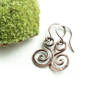 May include: A pair of copper wire earrings with a hammered finish. The earrings are shaped like a double spiral.