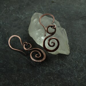 May include: A pair of copper wire earrings with a spiral design. The earrings are handmade and have a rustic, organic look.