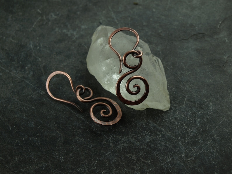May include: A pair of copper wire earrings with a spiral design. The earrings are handmade and have a rustic, organic look.