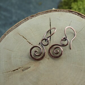 May include: A pair of copper earrings with a spiral design. The earrings are handmade and have a rustic look.