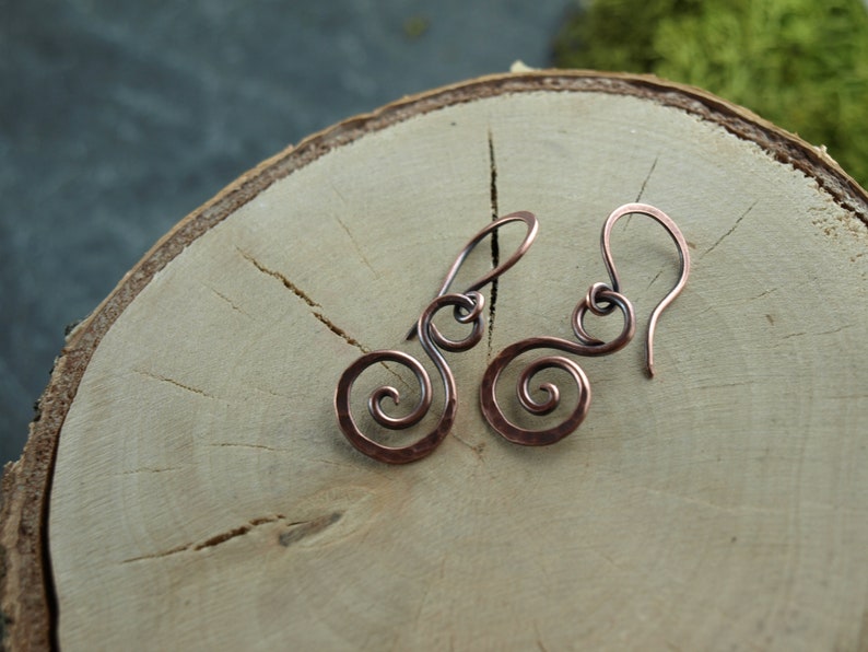 May include: A pair of copper earrings with a spiral design. The earrings are handmade and have a rustic look.