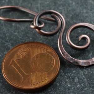 May include: A hammered copper wire earring with a spiral design. The earring is shown next to a 1 cent euro coin for scale.