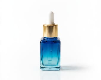May include: A small, square glass bottle with a blue gradient, topped with a gold cap and a white dropper. The bottle is designed for skincare products and sits on a white surface.