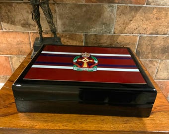 May include: A black wooden box with a red, white, and blue striped lid. The lid features a crest with a crown, cross, and the word "GRAVESEND".