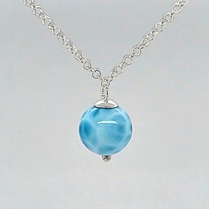 May include: A silver chain necklace with a light blue round pendant. The pendant has a swirling pattern.
