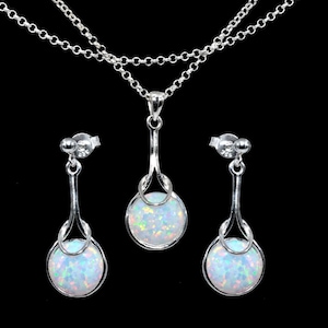 May include: A silver-toned jewelry set featuring a necklace and a pair of earrings. The necklace has a double chain and a pendant with a round, iridescent opal. The earrings mirror the pendant design, each with a post back.