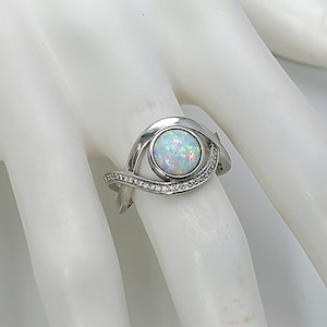 May include: A silver ring with a white opal gemstone and a row of small clear stones on the band.