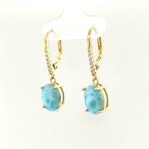 May include: Gold earrings with a light blue oval gemstone and a row of clear cubic zirconia stones on the dangle.