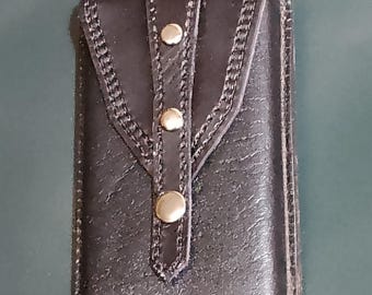 May include: A black leather phone case with a flap closure and silver metal accents. The case has a stitched design around the edges.