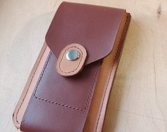 May include: A brown leather phone case with a tan leather trim and a silver button closure.