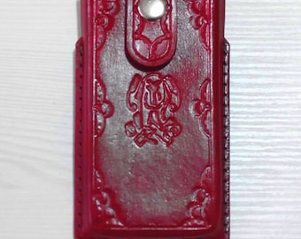 May include: A crimson leather phone case with an embossed design. The case has a snap closure and a detailed floral and scroll pattern. The leather has a slightly distressed appearance.