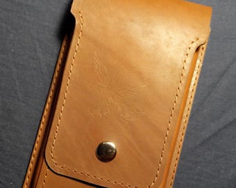 May include: A tan leather phone case with a flap and a silver press stud. The case features a stitched edge and a delicate embossed pattern. The rectangular case appears to be handmade.