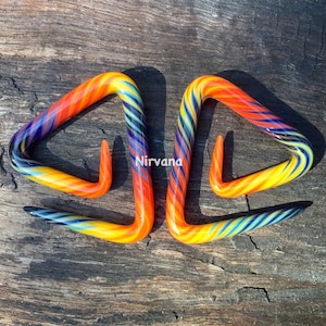 May include: Two colorful glass ear gauges in the shape of a triangle. The gauges are a mix of yellow, orange, blue, and purple.