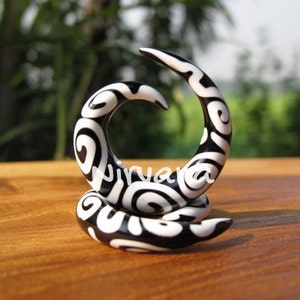 以下が含まれることがあります： アクリル製の黒と白の渦巻き型のイヤーゲージ。ゲージは渦巻き模様のデザインです。