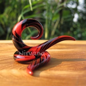 May include: A black and red glass spiral ear cuff. The spiral is made of glass and has a black and red swirl pattern.