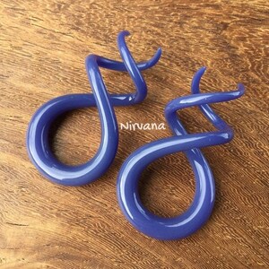 May include: Two purple glass spiral ear gauges. The gauges are twisted and have a circular shape.