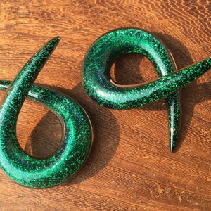 K&ouml;nnte beinhalten: Ein Paar gr&uuml;ne Glitzer-Spiral-Ohrenstretcher. Die Stretcher sind aus Acryl und haben eine gl&auml;nzende, glitzernde Oberfl&auml;che.