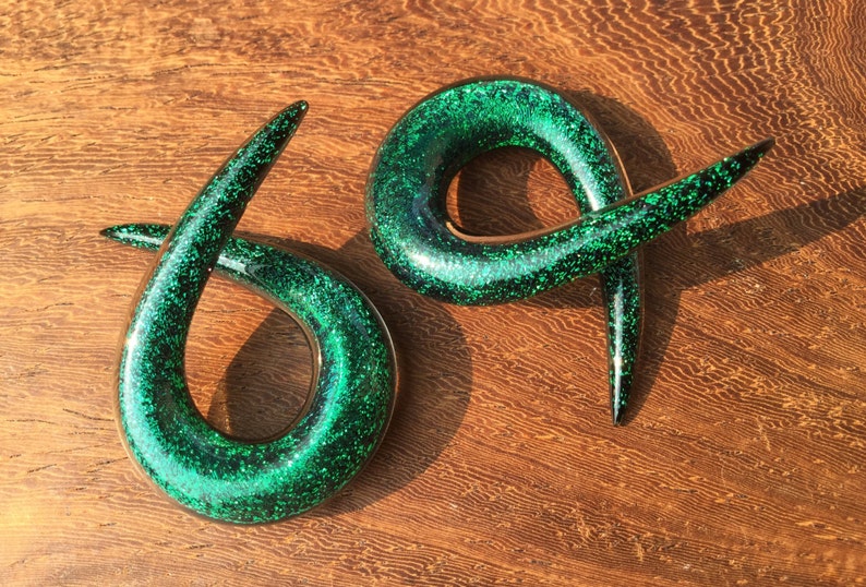K&ouml;nnte beinhalten: Ein Paar gr&uuml;ne Glitzer-Spiral-Ohrenstretcher. Die Stretcher sind aus Acryl und haben eine gl&auml;nzende, glitzernde Oberfl&auml;che.